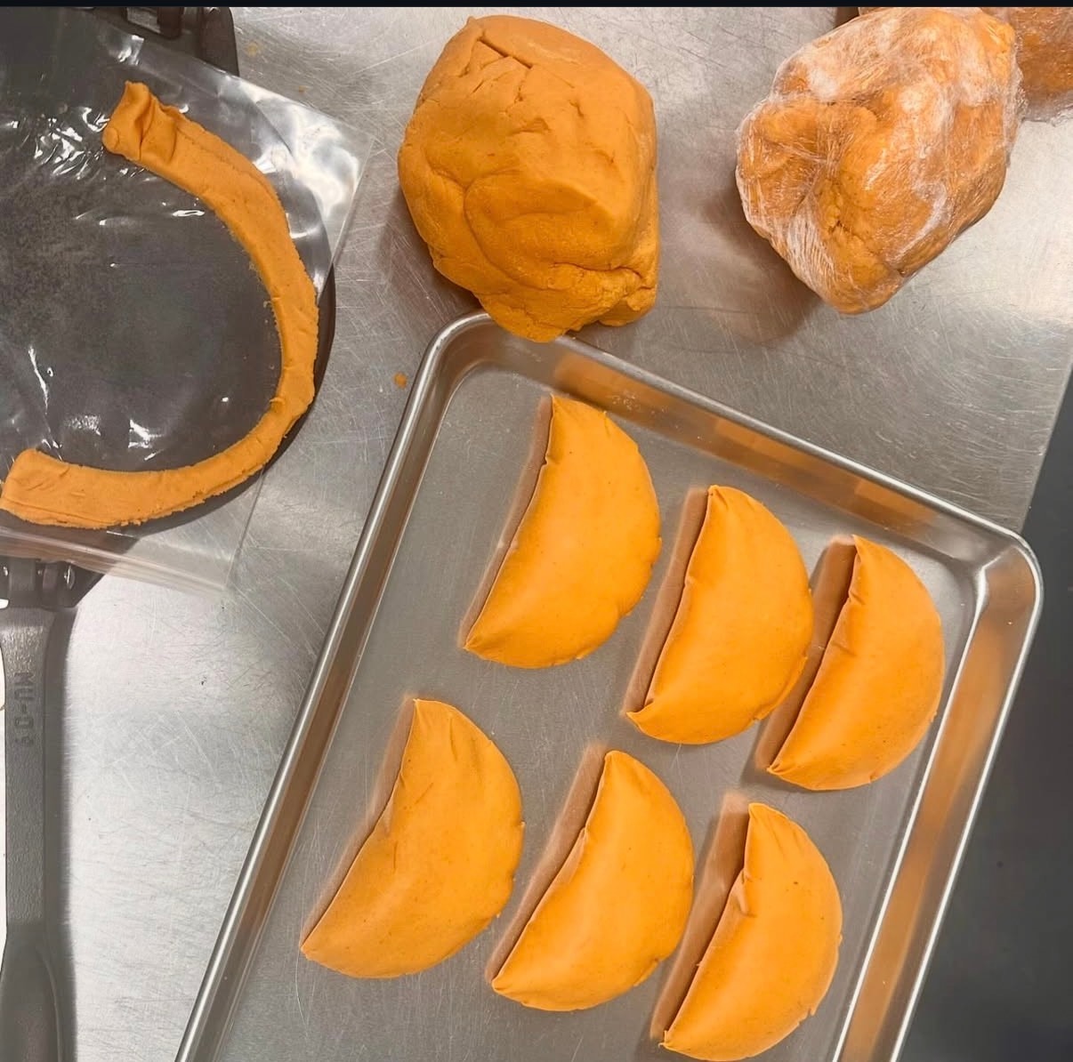Raw dough balls and shaped empanadas on a sheet tray — the masa process